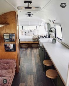 the interior of a camper with wood flooring and white counter tops, along with wooden stools