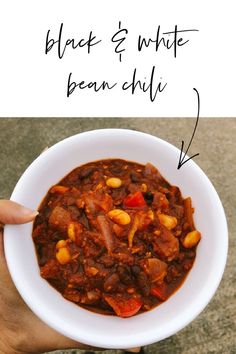 a hand holding a white bowl filled with chili and beans next to the words black & white bean chili