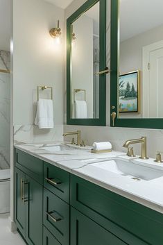 a bathroom with two sinks, mirrors and green cabinetry on the countertop in front of a white toilet