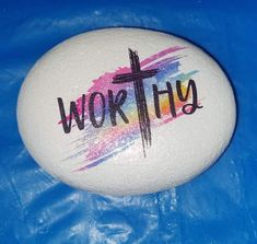 a painted rock with the word worthy written on it and a cross in the center