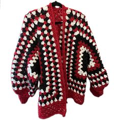 a red and black crocheted cardigan is hanging on a white hanger