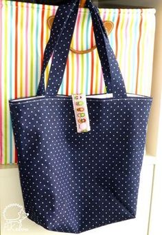 a blue polka dot tote bag hanging on a wall with colorful striped curtains behind it