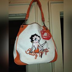 This Is A Poppin' Orange And Taupe Denim Costume Character Bag With A Picture Of Betty Boop In Colorful Patent Leather Beige And Black Picture And Her Name Spelled Under A Burlesque Style Sitting Position, Reinforced With Leather Straps, Heavy Silver Metal Clamps And Cornered Leather Upside Down Triangle Edges Lining Also In And Around The Leather, On The Inside Is A Polyester Teal Aqua Beautiful Orange Burst Lip Prints Lining The Zippers And Orange Fastening The Big Bold *B* Silver Ring Zipper Handle And Inner Clamps Bordering The Leather Orange Material. It Is Slightly Dingy In Areas That Can Be Brushed Out With A Toothbrush Cold Water And Mild Soap Or Dishwashing Liquid I Wouldn't Sugges Black Picture, Lips Print, Orange Cream, Orange Leather, Character Costumes, Betty Boop, Patent Leather, Metallic Silver, Leather Straps