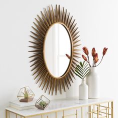 a white table topped with a mirror and vase filled with flowers next to a gold shelf