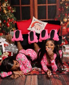 two women in pink pajamas laying on the floor with christmas decorations and presents behind them