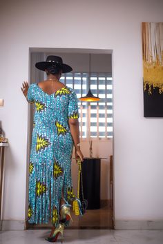 A woman posing in a blue and green African Print maxi dress with frills. Blue Floor-length Maxi Dress For Summer, Casual Ruffled Maxi Dress, Casual Long Ruffled Maxi Dress, Casual Maxi Dress With Ruffles, Blue Ruffled Floor-length Maxi Dress, Ruffled Maxi Dress For Vacation, Blue Floor-length Ruffled Maxi Dress, Blue Floor-length Maxi Dress With Ruffles, Printed Long Dress For Vacation