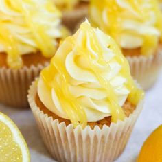 cupcakes with white frosting and lemon wedges on a table next to an orange slice