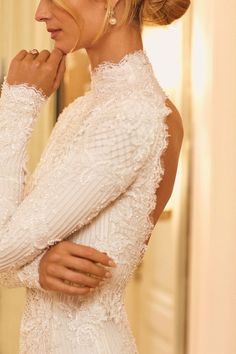 a woman in a white dress looking at herself in the mirror with her hand on her chin