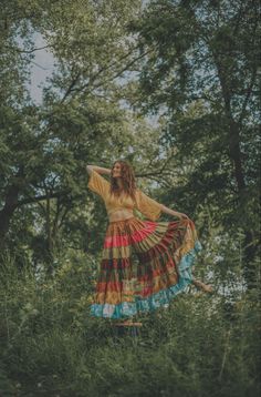 a woman is standing in the grass with her arms behind her back, wearing a colorful dress