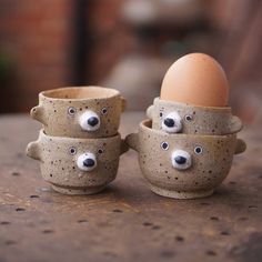 three egg cups with faces on them sitting on a table next to an egg in the shape of bears