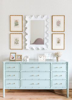 a blue dresser with pictures on the wall above it and a framed mirror over it