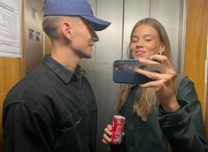 a man and woman taking a selfie in an elevator with a can of soda