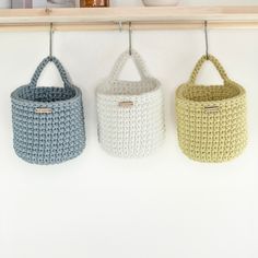 three crocheted baskets hanging on a wall in front of a coffee pot and mug