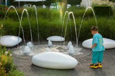 a young boy standing in front of a fountain with water spouting from it