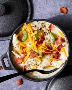 a skillet filled with cheese, bacon and green peppers next to other cooking utensils