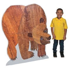 a young boy standing next to a wooden bear cutout