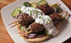 a plate topped with meatballs and veggies on skewered sticks next to cucumbers