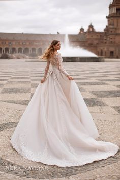 a woman in a white wedding dress standing on a stone floor with a fountain behind her