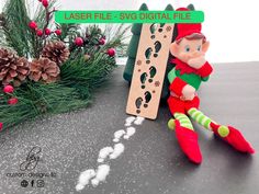 an elf is sitting next to a christmas tree with footprints on it and a laser file