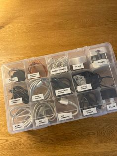 an open plastic box filled with different types of cords and plugs on top of a wooden table