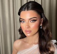 a woman with long dark hair wearing an off shoulder white dress and diamond earrings on her head