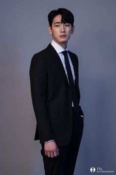 a young man in a suit and tie poses for a photo against a gray background