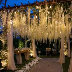 an outdoor wedding with white flowers hanging from the ceiling and candles lit up on the ground