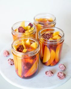 four jars filled with fruit and nuts on top of a white plate next to pink candies