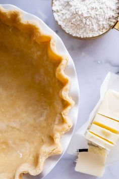 an uncooked pie crust next to butter and other ingredients on a marble table