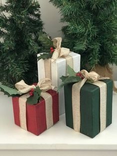 three wrapped presents sitting on top of a white shelf next to evergreens and pine cones