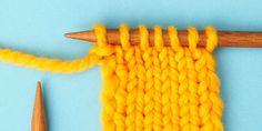 an orange knitted piece next to a wooden knitting needle on a light blue background