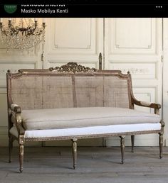 an antique style couch with white cushions and gold trimmings, in front of a chandelier