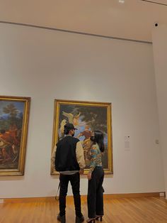 two people looking at paintings in an art gallery