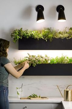 a woman standing in front of a kitchen counter with plants growing on the wall above her