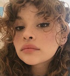 a close up of a person with curly hair and piercings on her nose looking at the camera