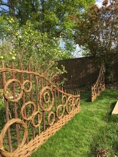 an iron fence made out of wood and wire in the grass next to a wooden bench