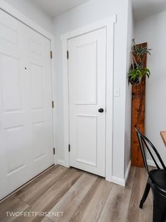 a room with two white doors and a black chair next to the door is a potted plant