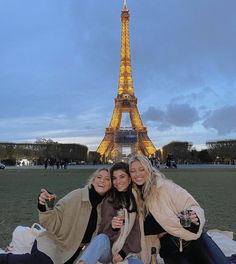 three women sitting on a blanket in front of the eiffel tower at night