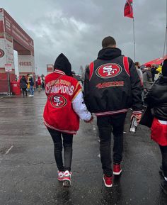 two people walking in the rain holding hands and wearing jackets with san francisco's logos on them