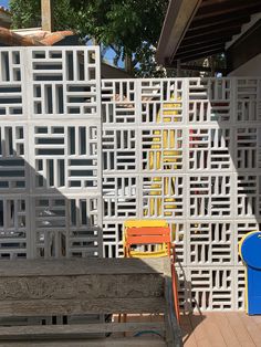 a wooden bench sitting in front of a white lattice wall with yellow and blue chairs