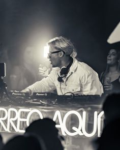 a man with headphones on sitting at a dj's desk in front of a crowd