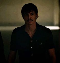 a man with a moustache standing next to another man in a dark room