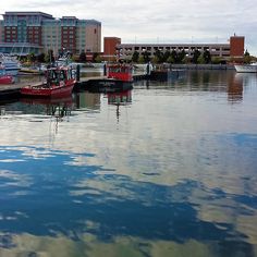 several boats are docked in the water near some buildings and clouds reflected in the water