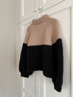 a sweater hanging on a door handle in front of a white door with a black and tan color block