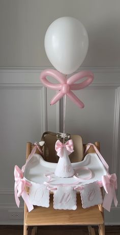 a baby's crib with a white balloon and pink bows on the top