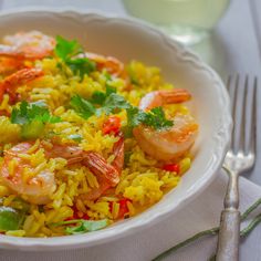 a white bowl filled with rice and shrimp on top of a table next to a fork