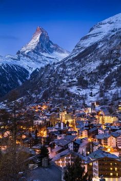 a town in the mountains at night with snow on the mountain tops and buildings lit up