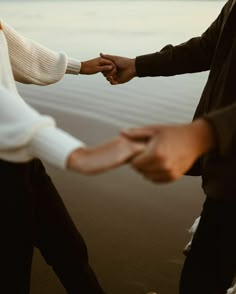 two people holding hands while standing on the beach