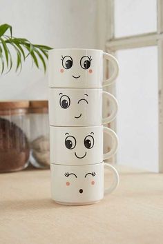 four coffee cups with faces drawn on them sitting on a table next to a potted plant