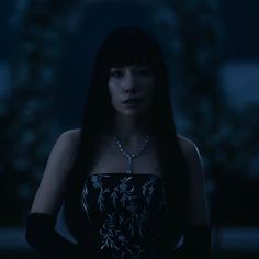 a woman with long black hair in a dark room wearing a dress and holding her hands behind her back